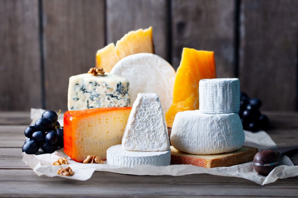 Cheese assortment: blue cheese, hard cheese, soft cheese on a parchment paper. Wooden background.