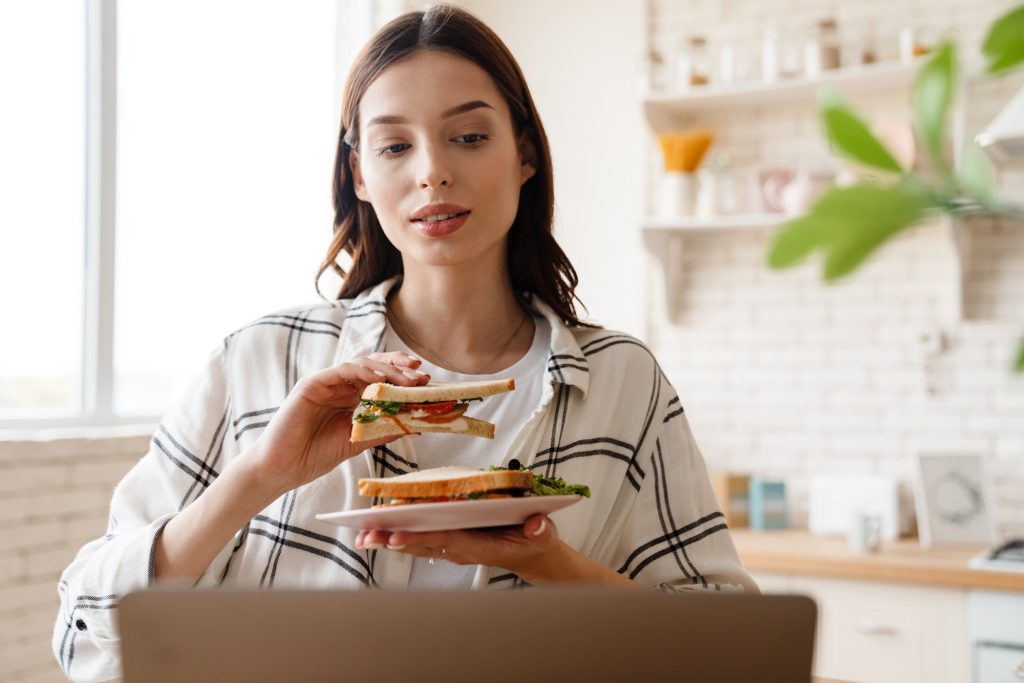 Beautiful focused woman working with laptop while eating sandwich